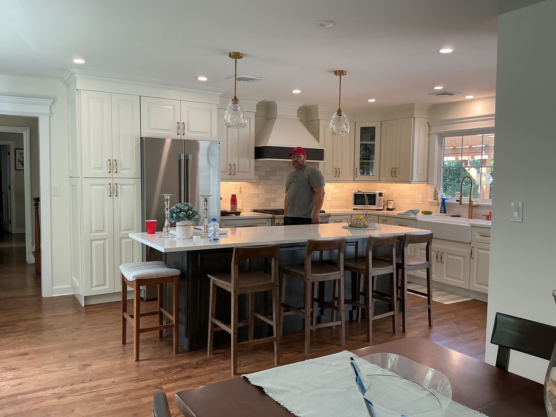 Bright white kitchen with a person at the island and hardwood floors; dining table in foreground.