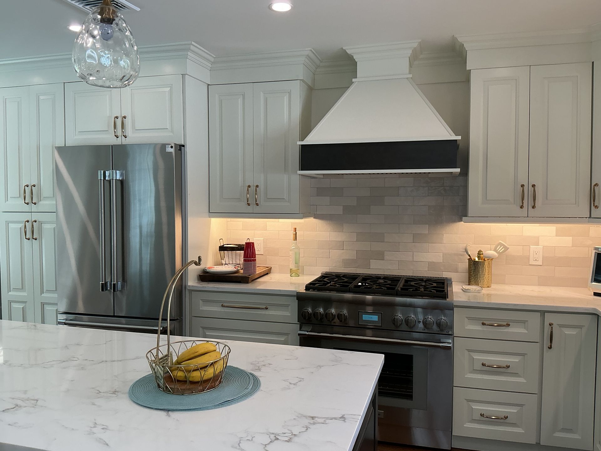 Bright white kitchen with stainless steel appliances and marble island, bananas on a blue plate