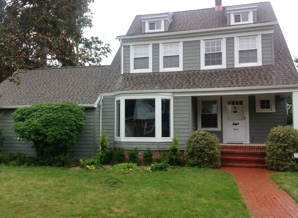 Green house with white trim, red brick walkway, and green lawn.
