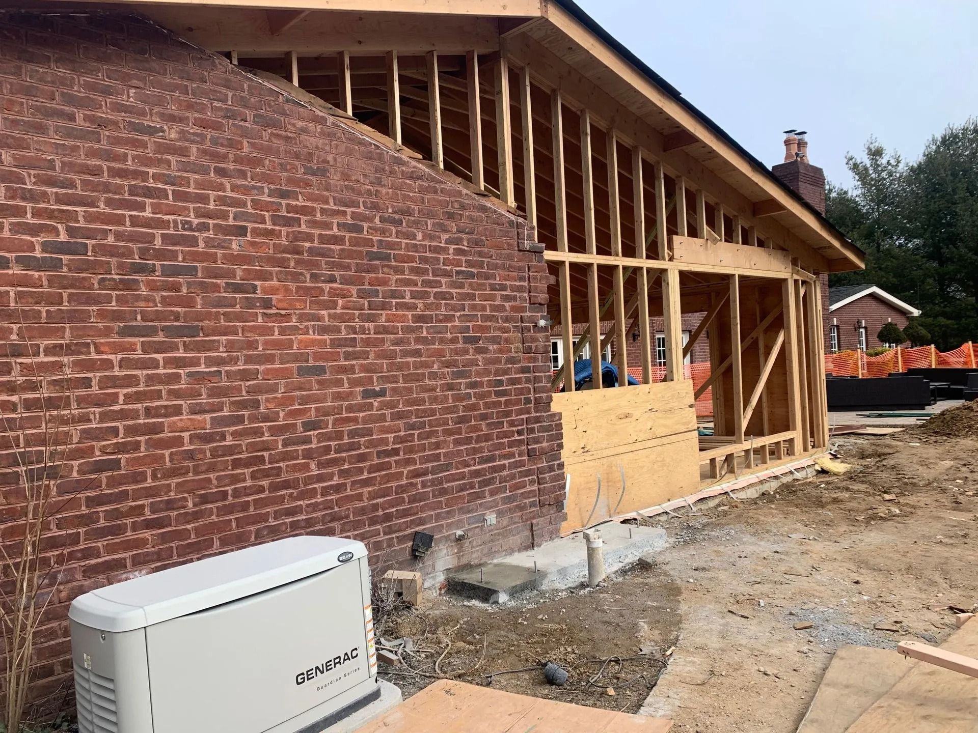 Exterior home under construction. Brick wall connects to a wood-framed addition. Generator in the foreground.