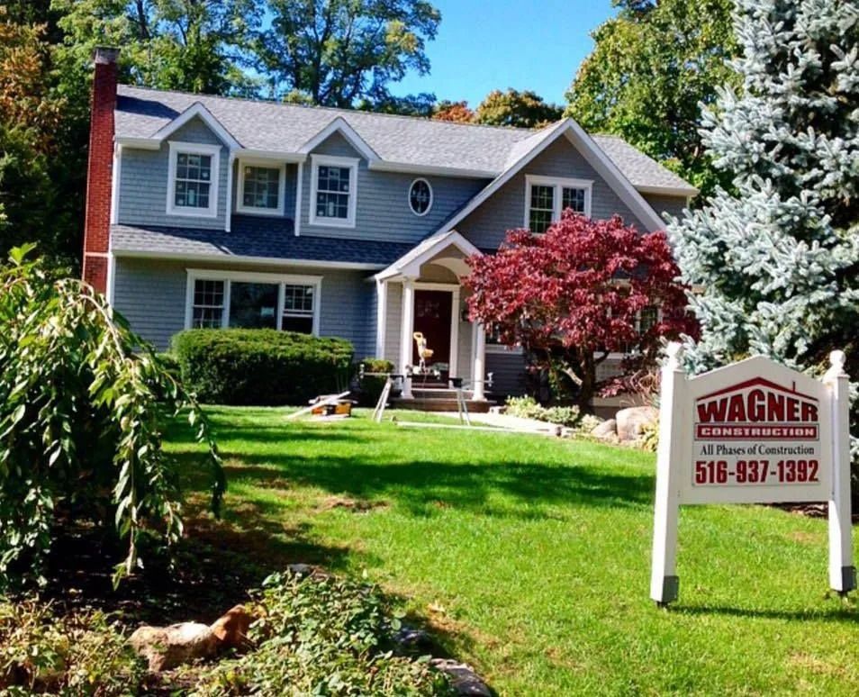 Gray house with green lawn, red tree, and Wagner Roofing sign.