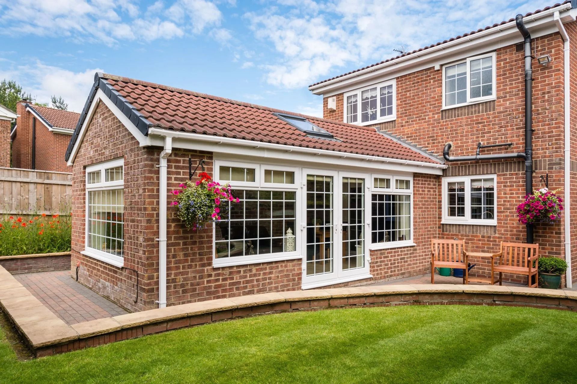 Brick home with red tile roof and glass-walled extension; green lawn and low brick wall in front.