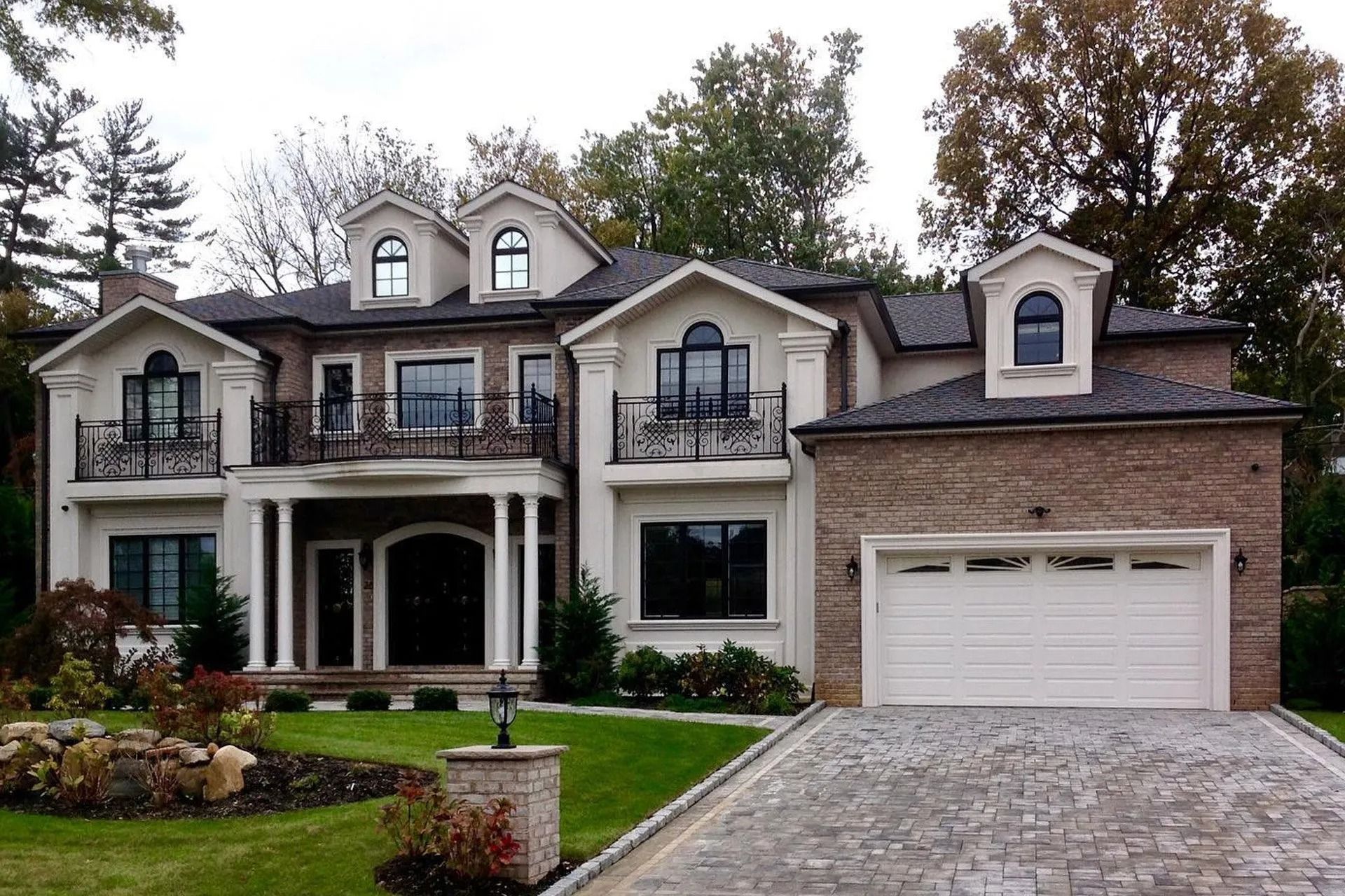 Two-story house with a brick and white facade, pillars, a garage, and landscaped lawn.