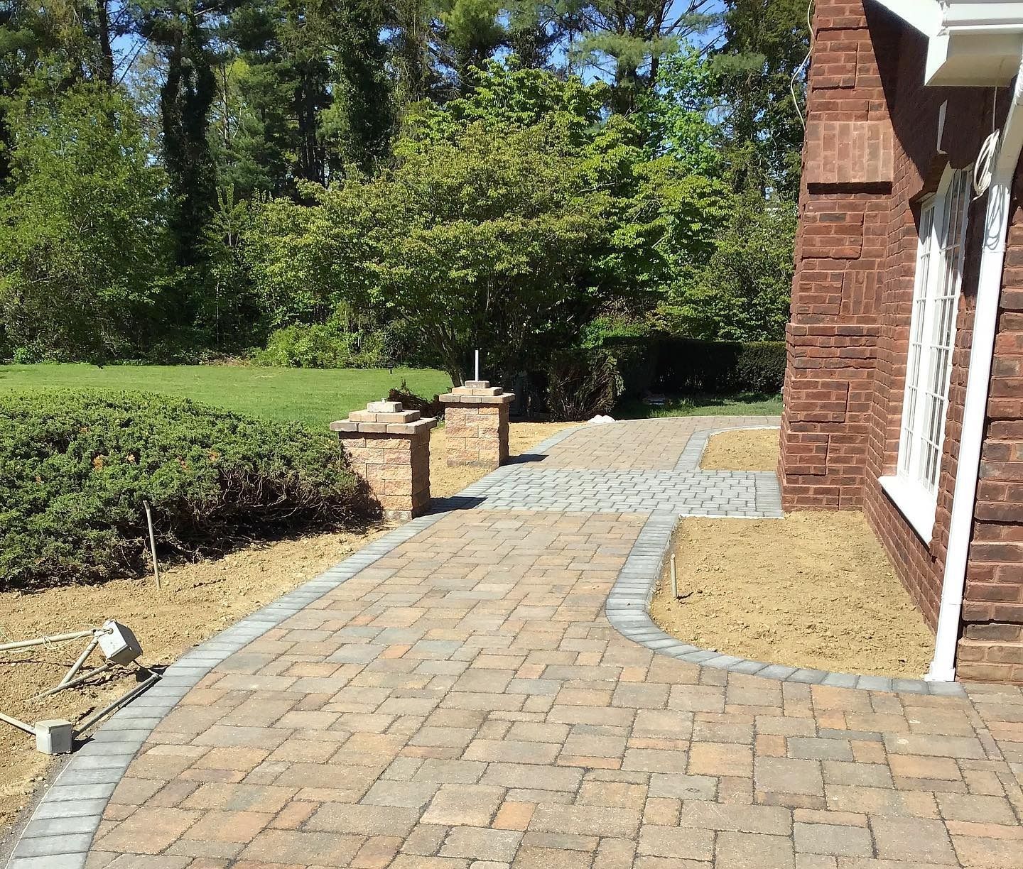 Brick walkway bordered by stone, leading toward a brick building and greenery.