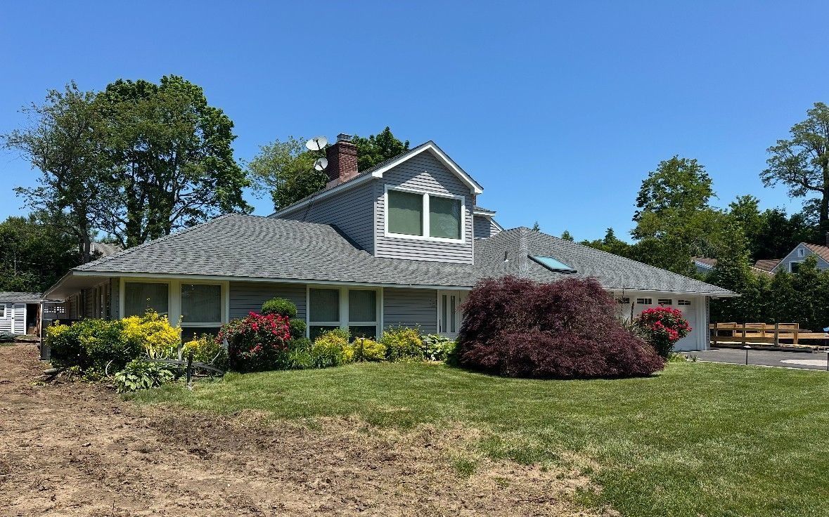 Gray house with gabled roof, light blue siding, and small front yard with bushes and green grass.