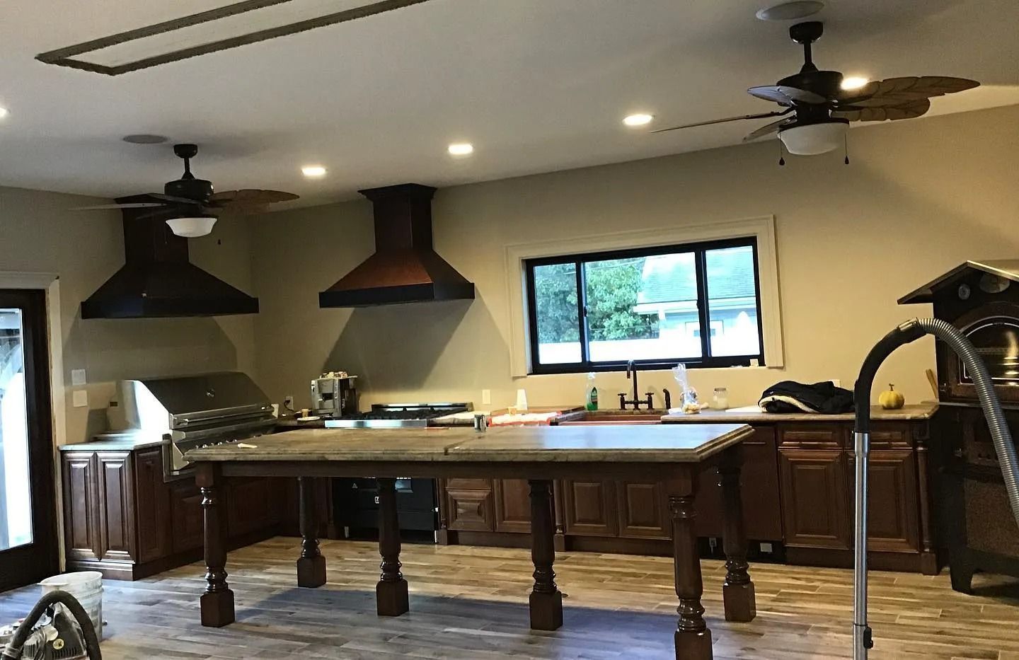 Kitchen with island, dark cabinets, stainless appliances, two range hoods, and ceiling fans.