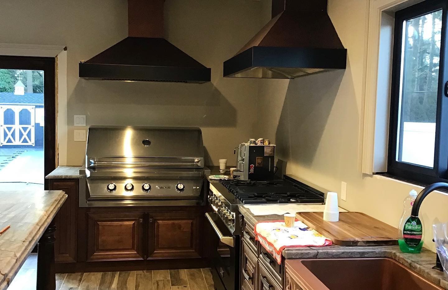 Outdoor kitchen with stainless steel grill, copper range hoods, and dark wood cabinetry.