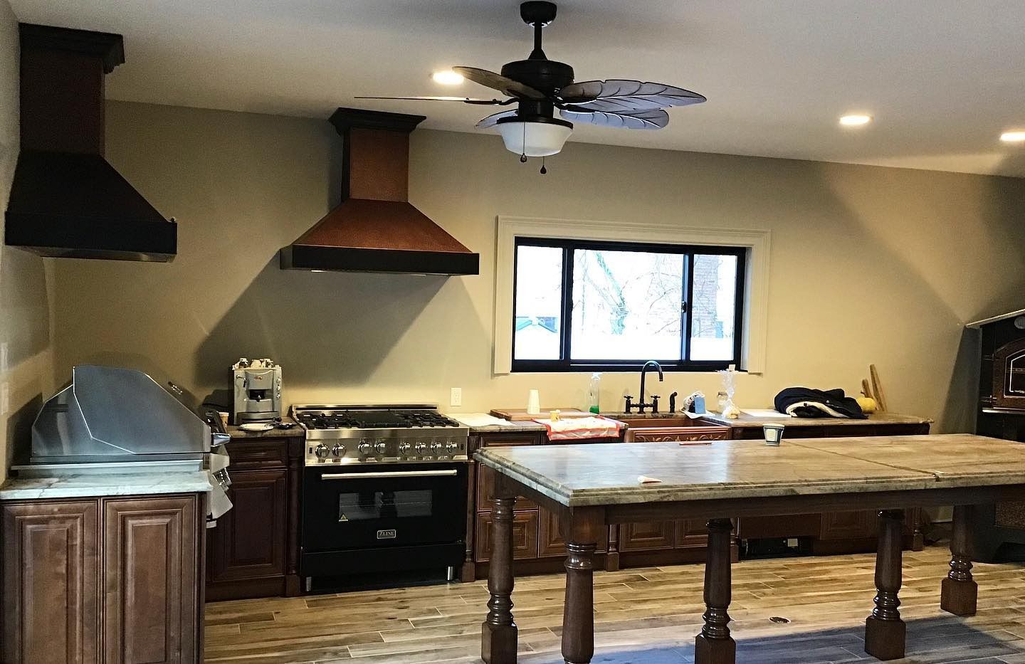 Kitchen with a stove, hood, island, and window. Brown cabinets, and wood range hood.