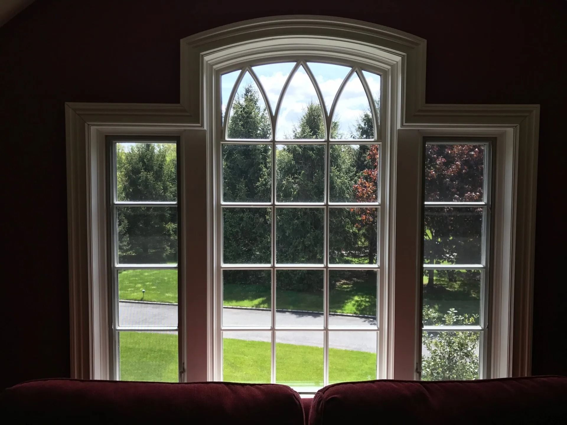 Window with white trim and a view of trees and a green lawn.