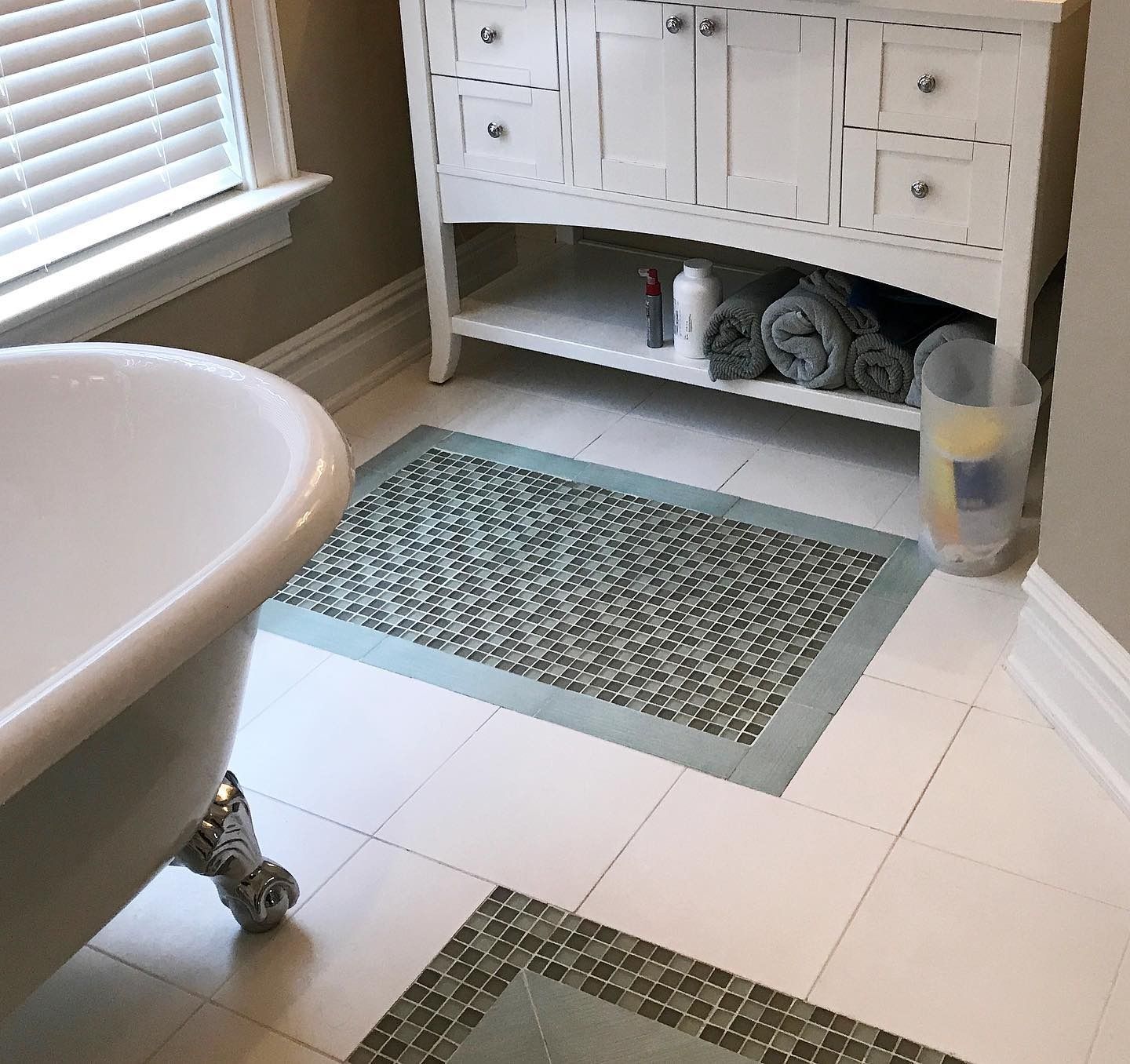 Bathroom with white tiled floor, white vanity, towels, and mosaic tile bath mats.