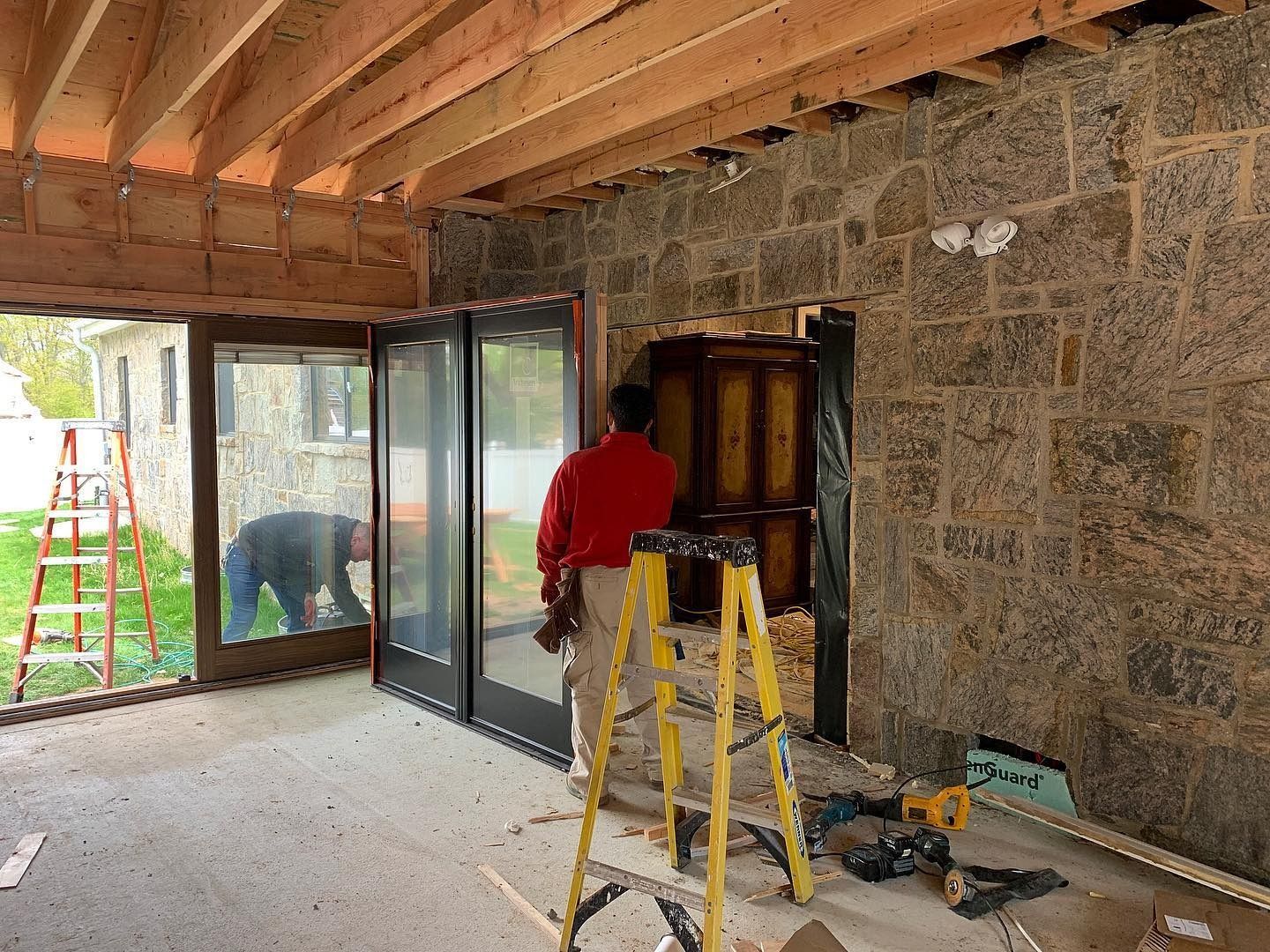Construction workers installing a door. One is inside, working on trim; another outside, visible through the glass door.