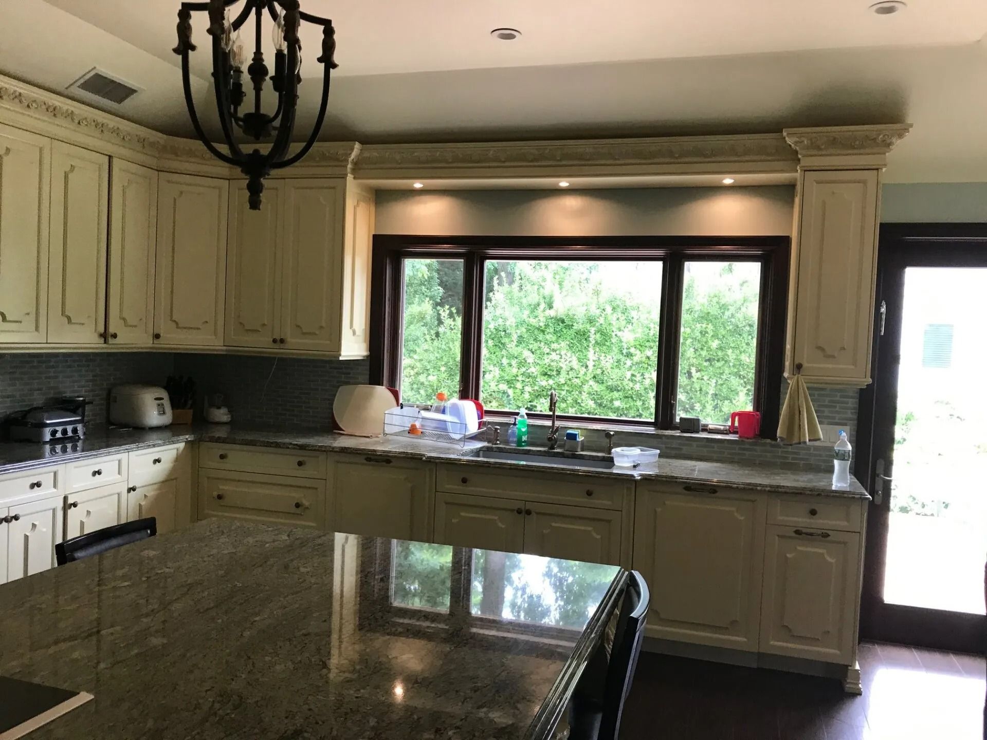 Cream-colored kitchen with granite countertops, a large window, and a dark chandelier.