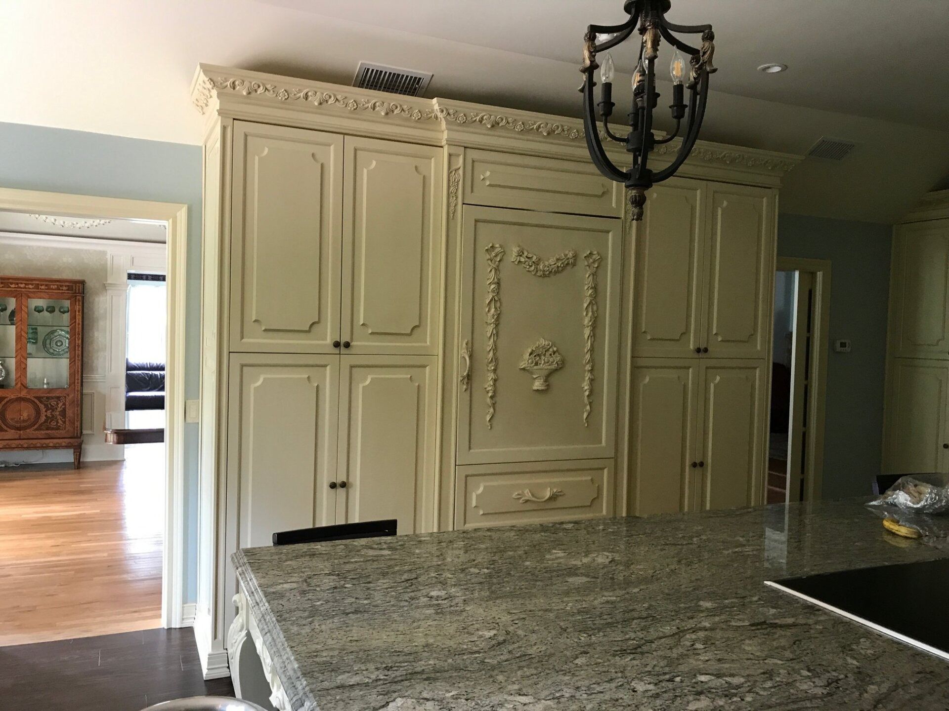 Cream-colored kitchen cabinets with ornate details, a granite countertop, and a black chandelier.