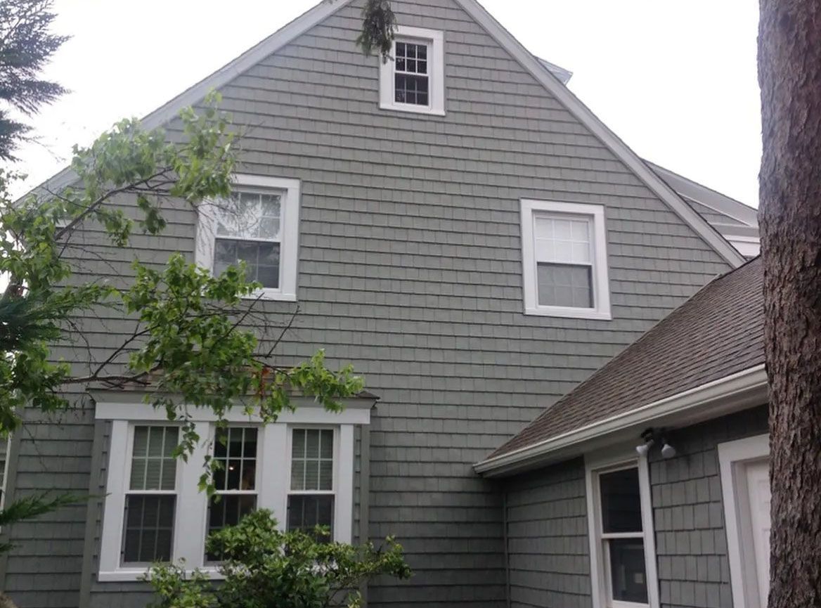 Grey shingled house with white window frames and small windows under a gable roof.