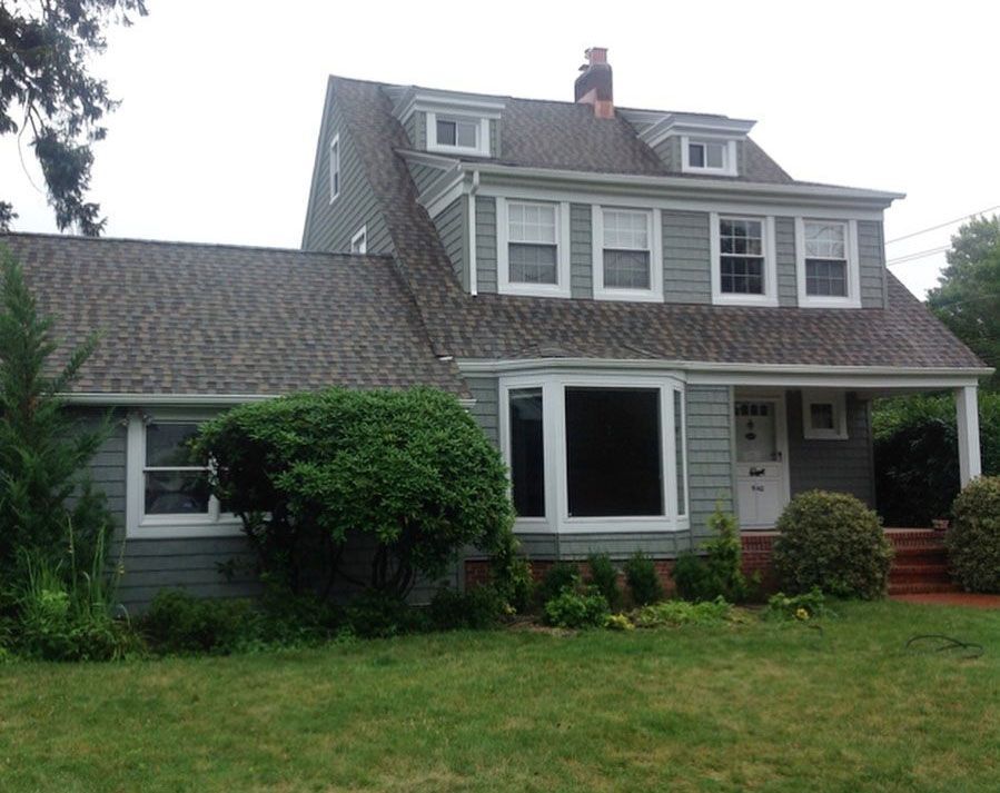 Two-story gray house with a gray roof and white trim. Bay window, small dormers, and green lawn.