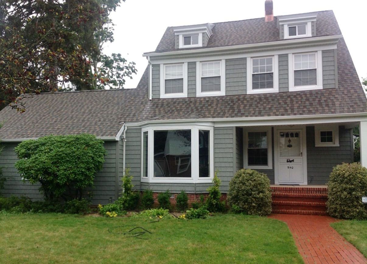Two-story house with green siding, brick walkway, and lawn, under a gray sky.