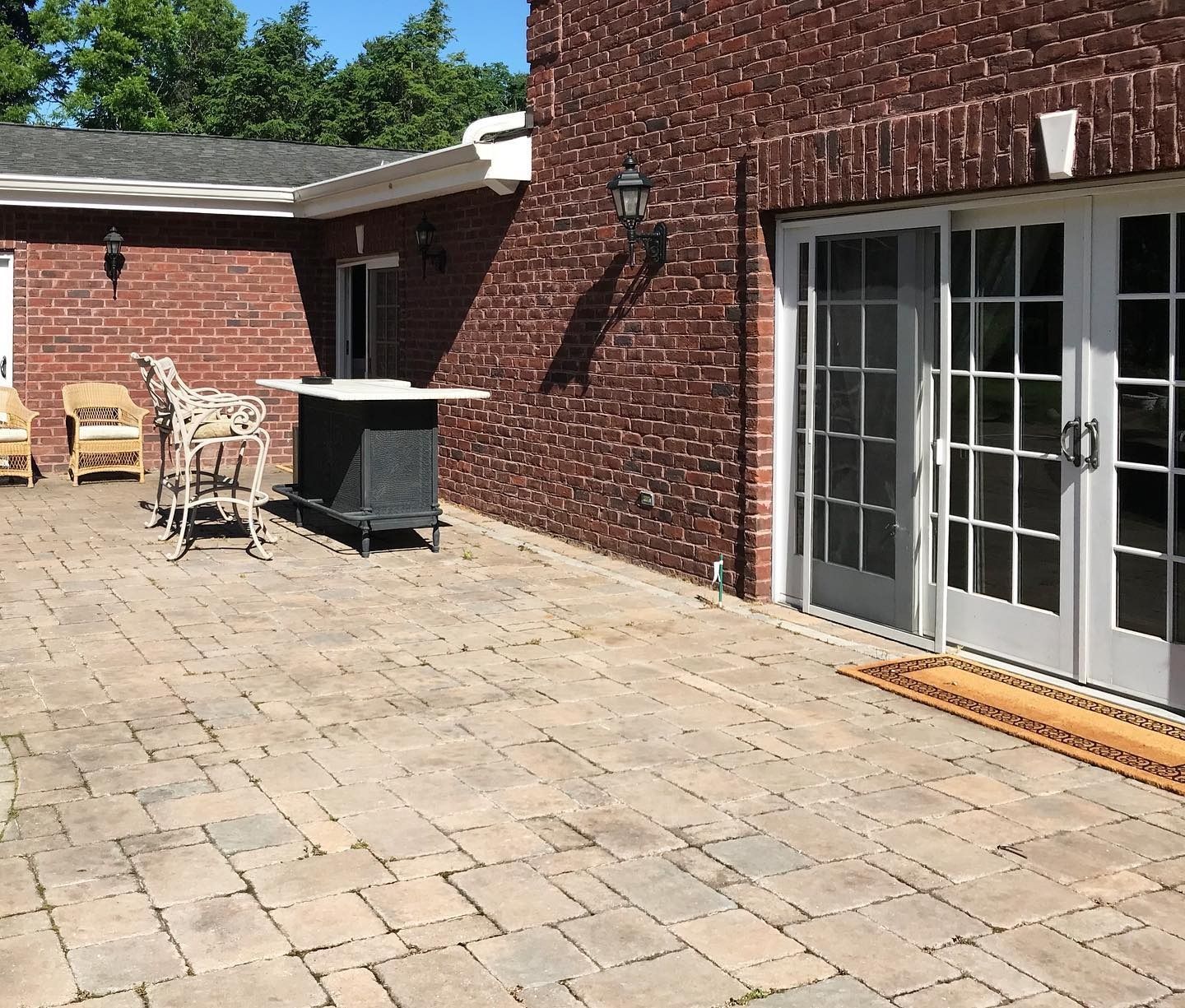 Brick patio with doors, furniture, and building in the background. Sunny day.