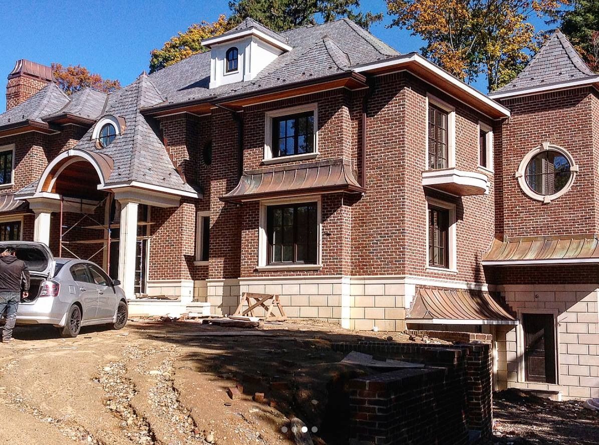 Large brick home under construction with gray roof and a car parked in front.
