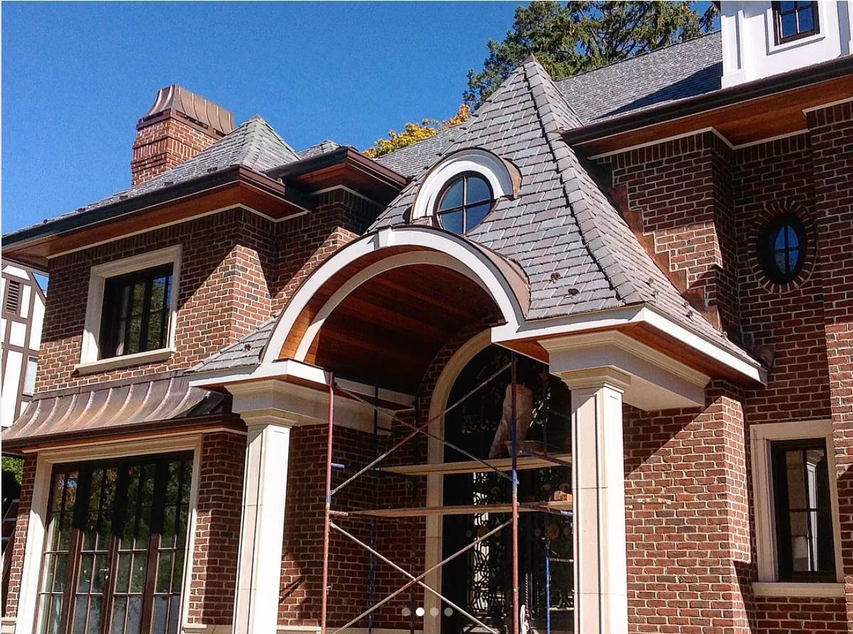 Brick house with arched entrance, columns, and a gray roof under a blue sky.