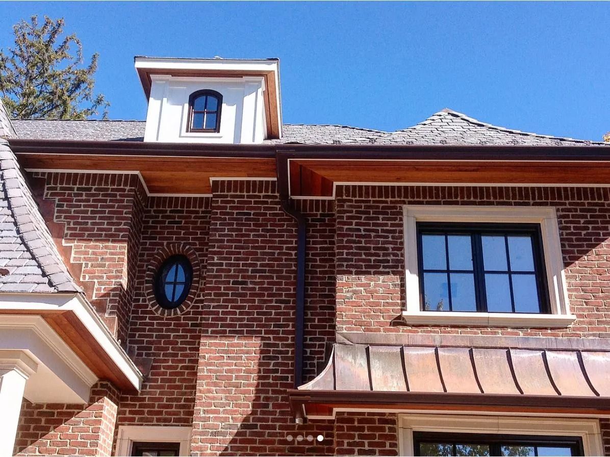 Brick building with dormer, wood trim, copper roof accents, and blue sky.