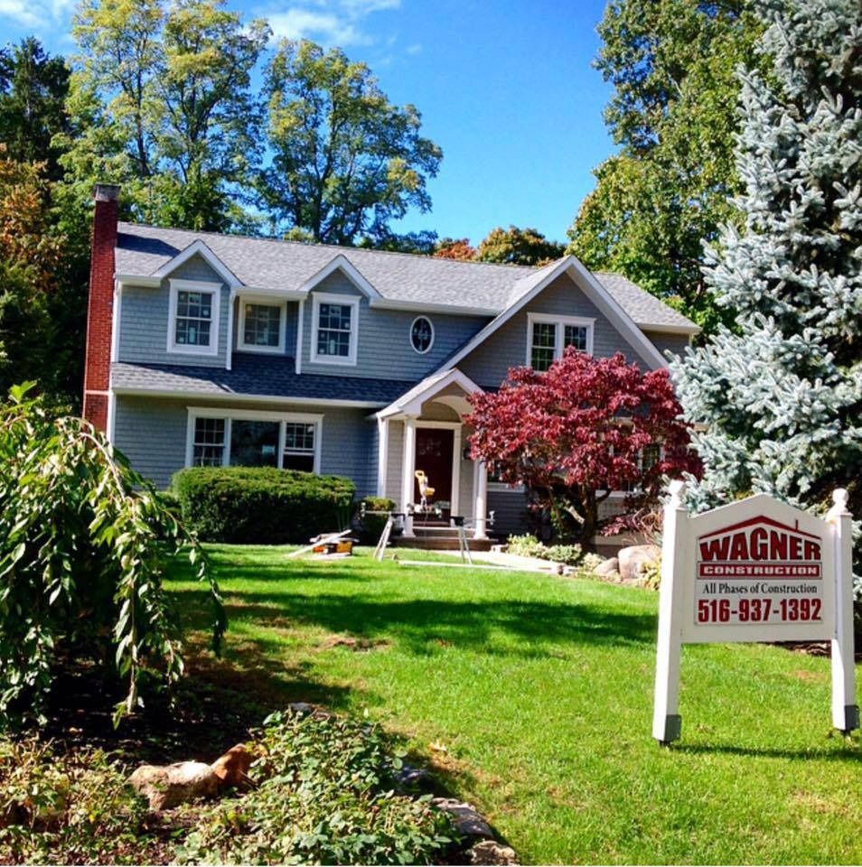 Gray house with dormers, red tree, green lawn, Wagner sign, sunny day.