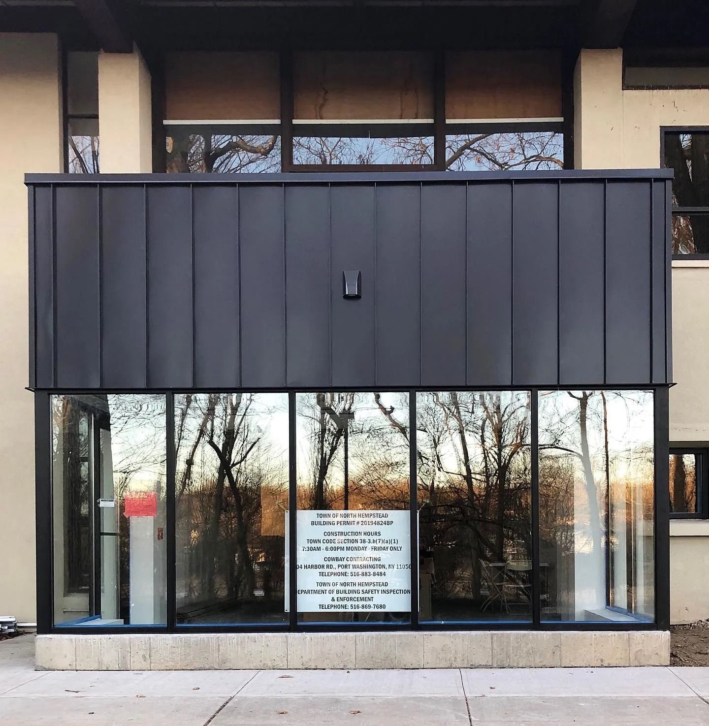 Building facade with black upper section, glass windows below reflecting trees. Signage visible.