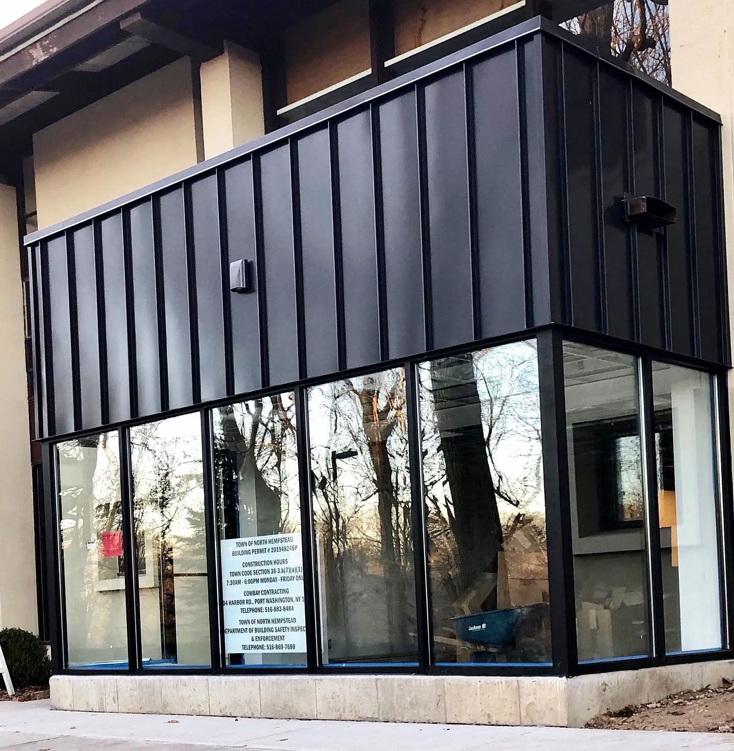 Black metal-clad structure with glass windows reflecting trees. A sign is visible.