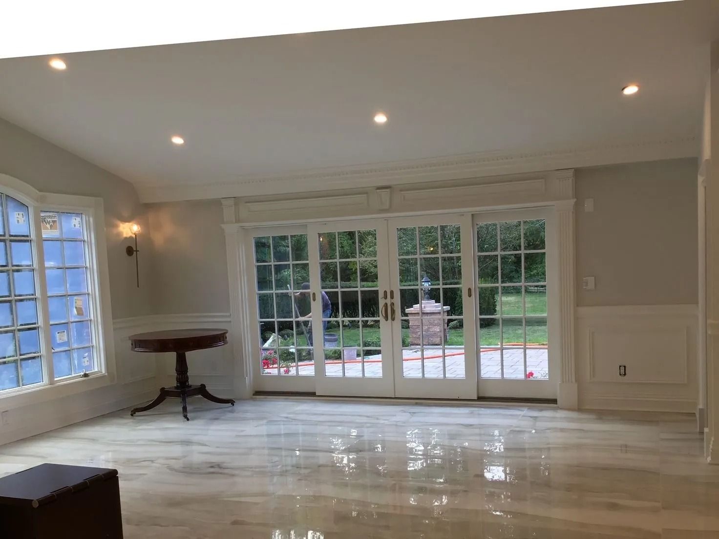 Bright room with glass doors, a round table, and shiny floor; leads to a garden.