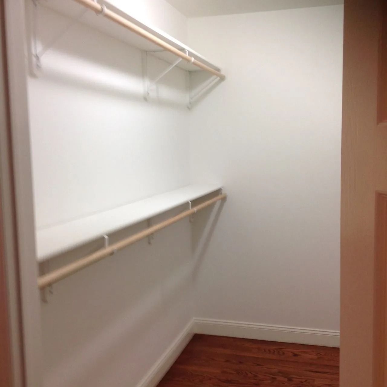 Empty white closet with a shelf and rod, wooden floor.