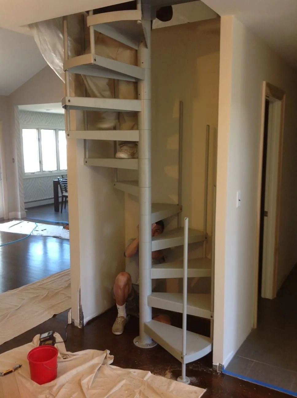 Spiral staircase in a corner, painted white. A person is visible. Paint supplies on floor.