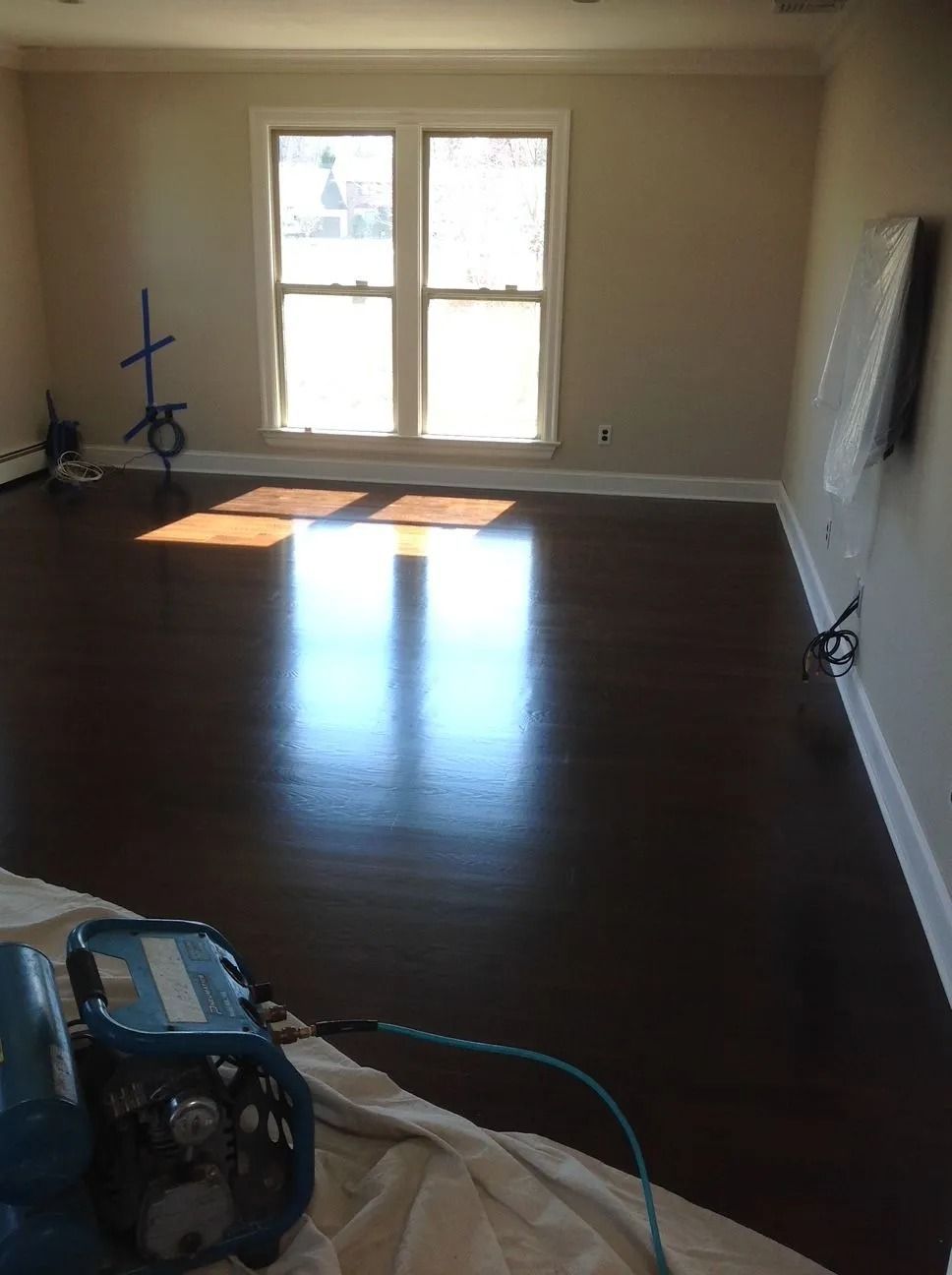 Dark wood floor reflecting sunlight in a room with a window. Tools are visible.