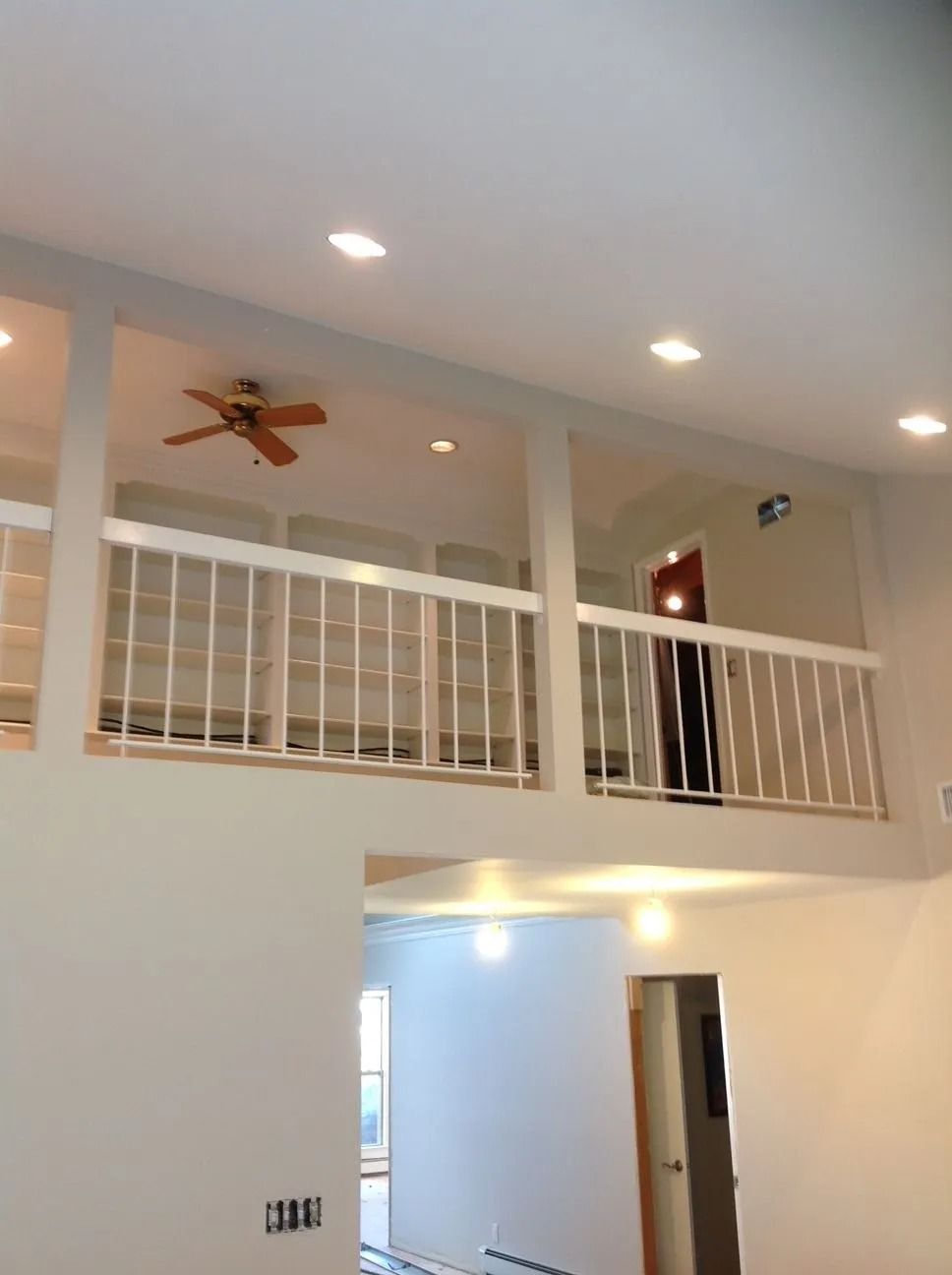 Interior view of a house with a loft, white railings, and recessed lighting. A ceiling fan is visible.