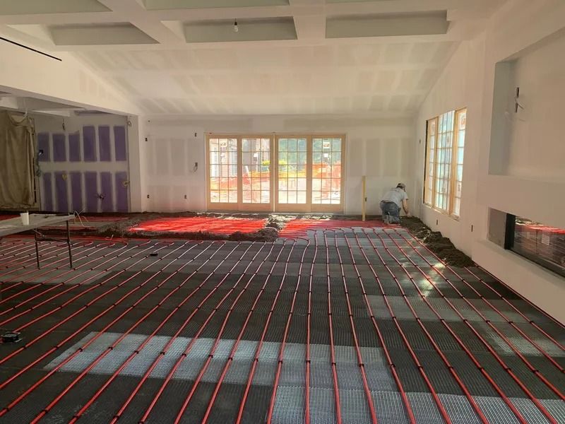 Interior room under construction with red radiant floor heating tubes installed. Person working near window.
