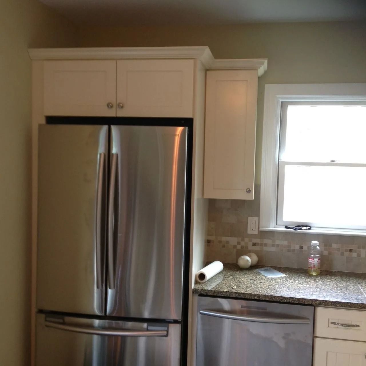 Stainless steel refrigerator in kitchen with overhead cabinets.