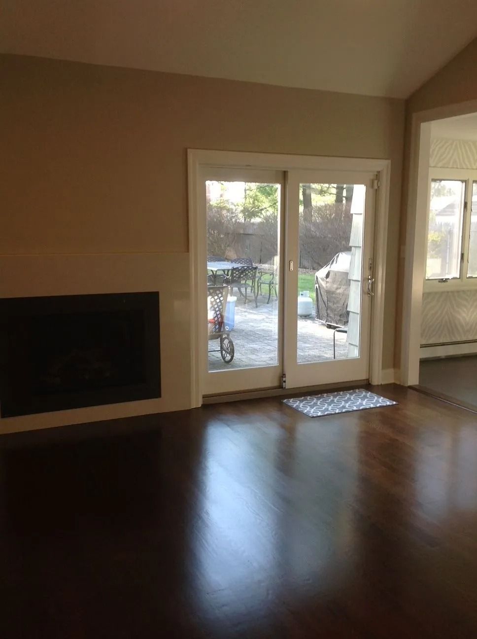 Living room with fireplace, sliding glass door to patio. Dark wood floor, beige walls.