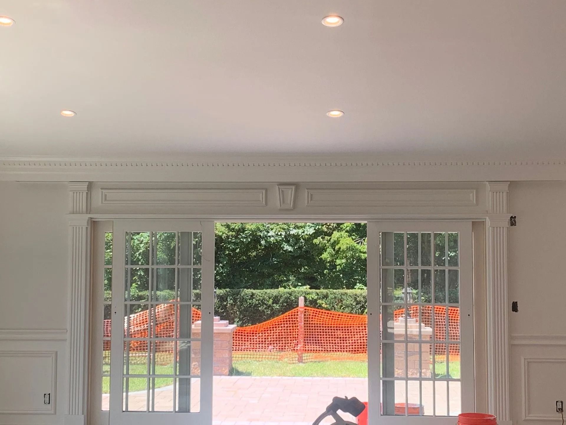 White-walled room with French doors opening to a backyard with orange barriers and greenery.
