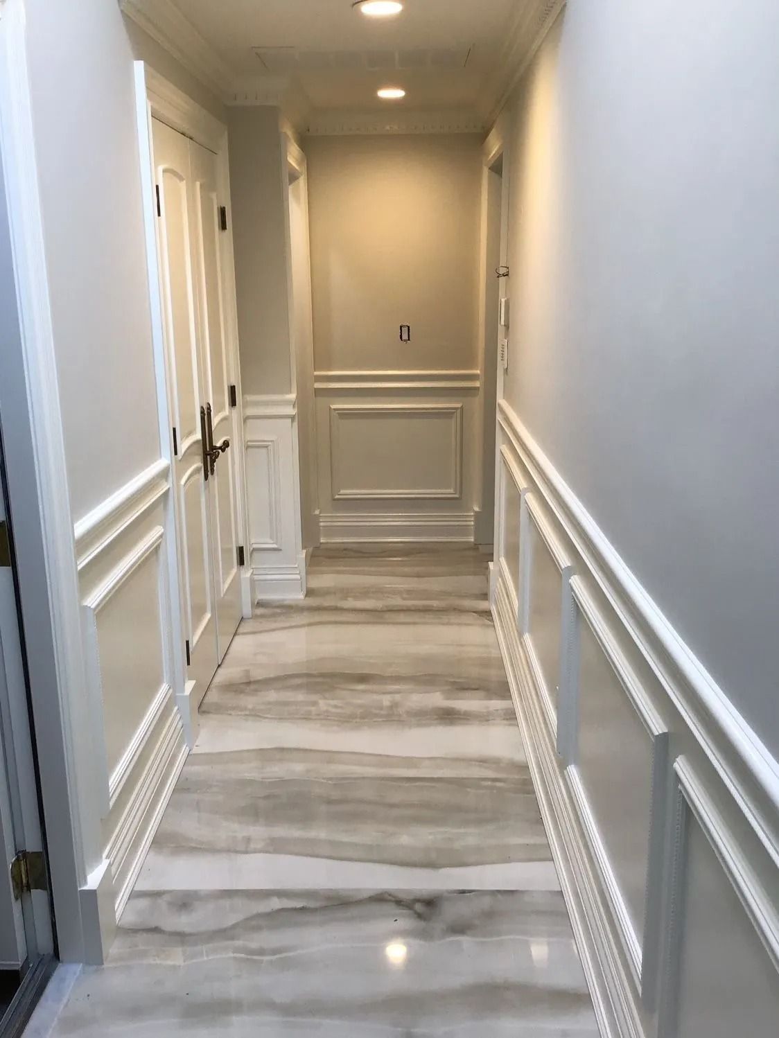 Hallway with white molding, light gray walls, and marble flooring. A door is on the left.
