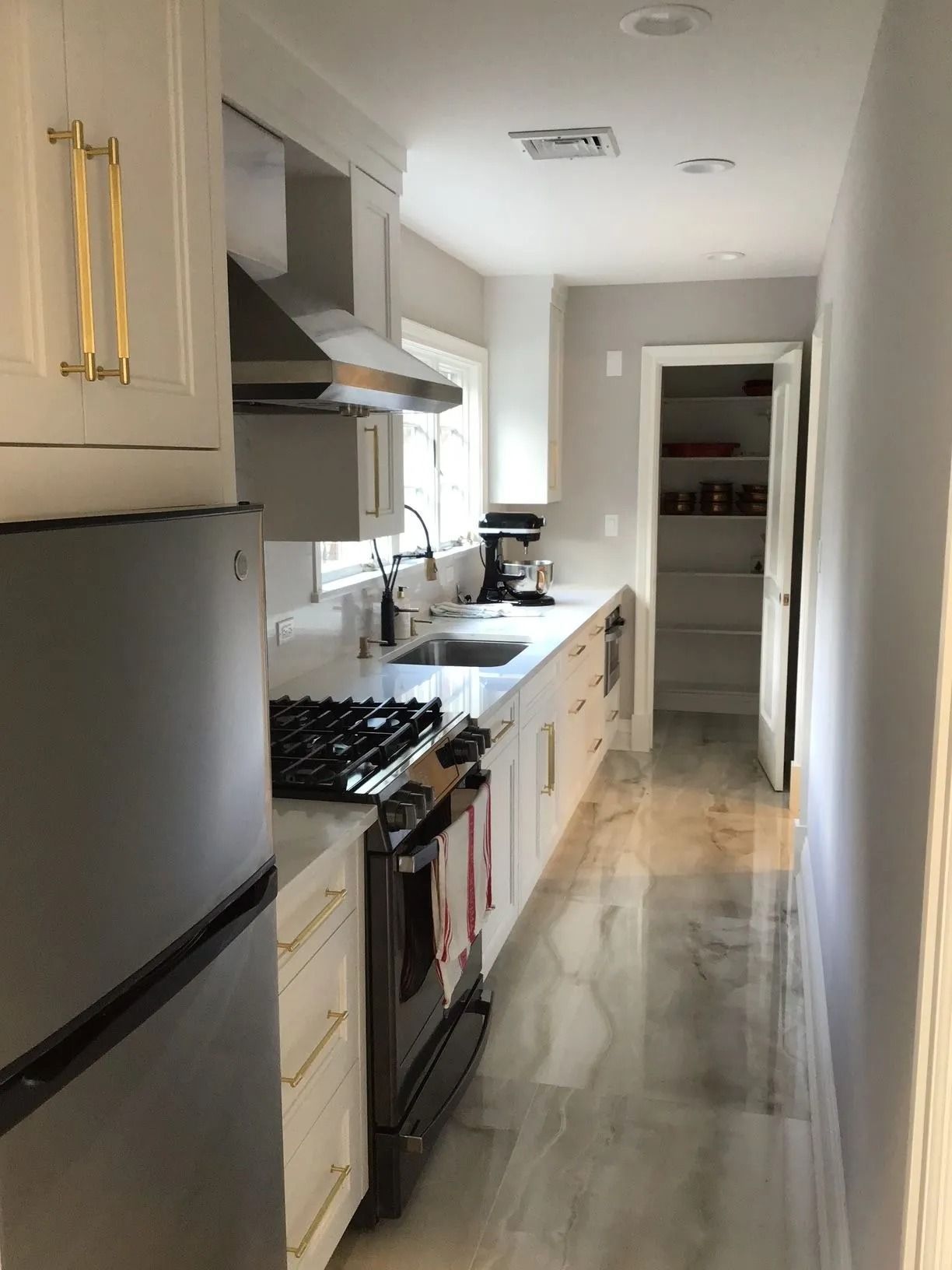 Long, narrow kitchen with white cabinets, stainless steel appliances, and a pantry.
