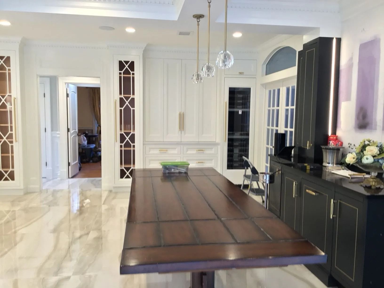 Luxurious kitchen with large brown island, white cabinets, marble floors, and decorative lighting.