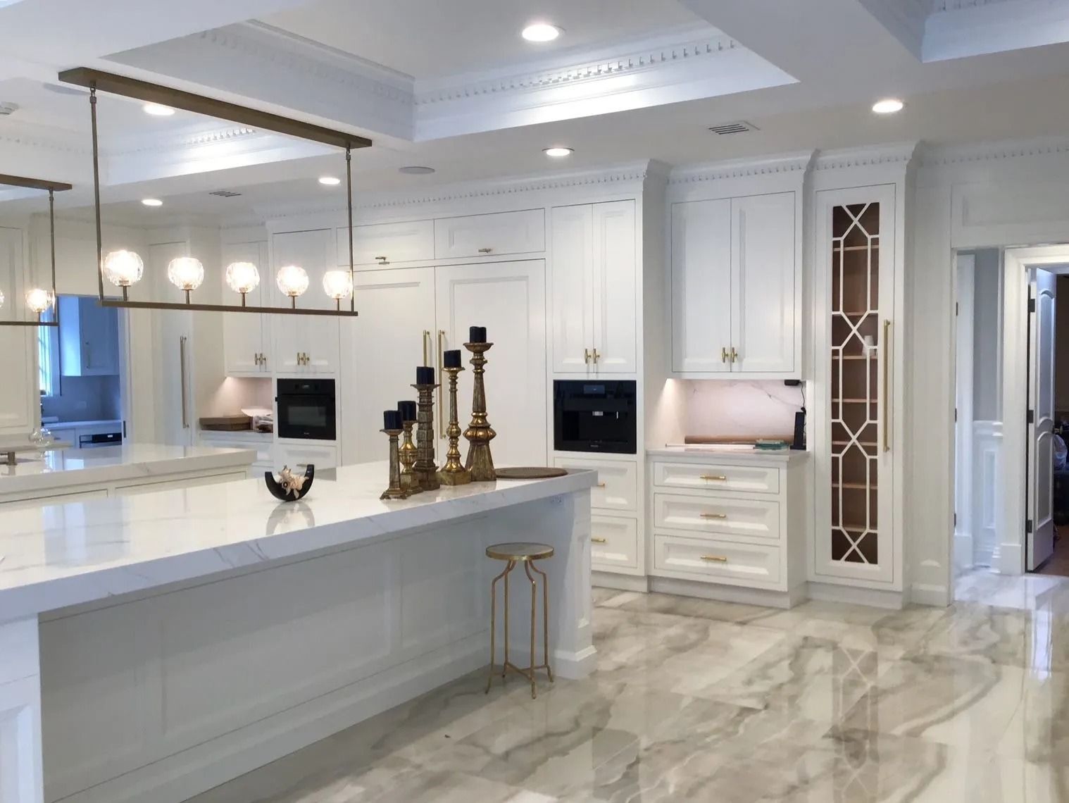 Modern white kitchen with marble floor, cabinets, island, and gold accents.