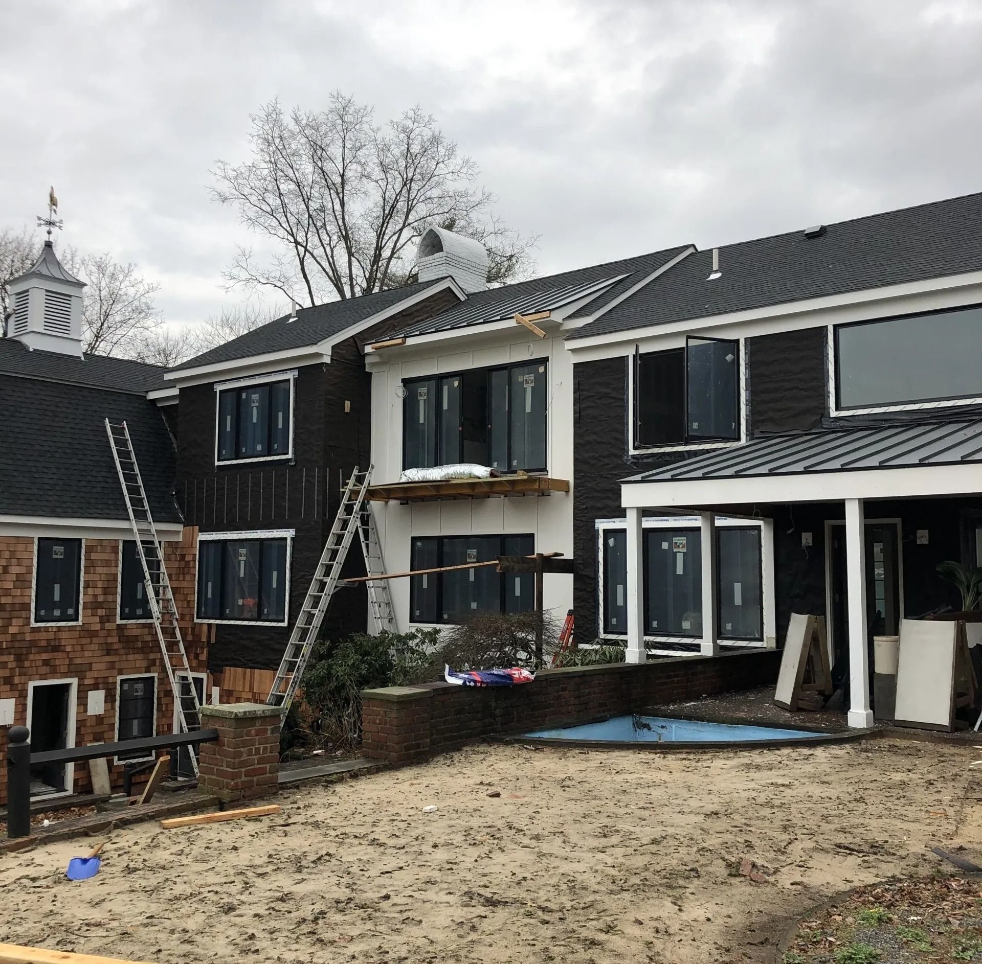House under construction with dark siding, new windows, and ladders on a cloudy day.