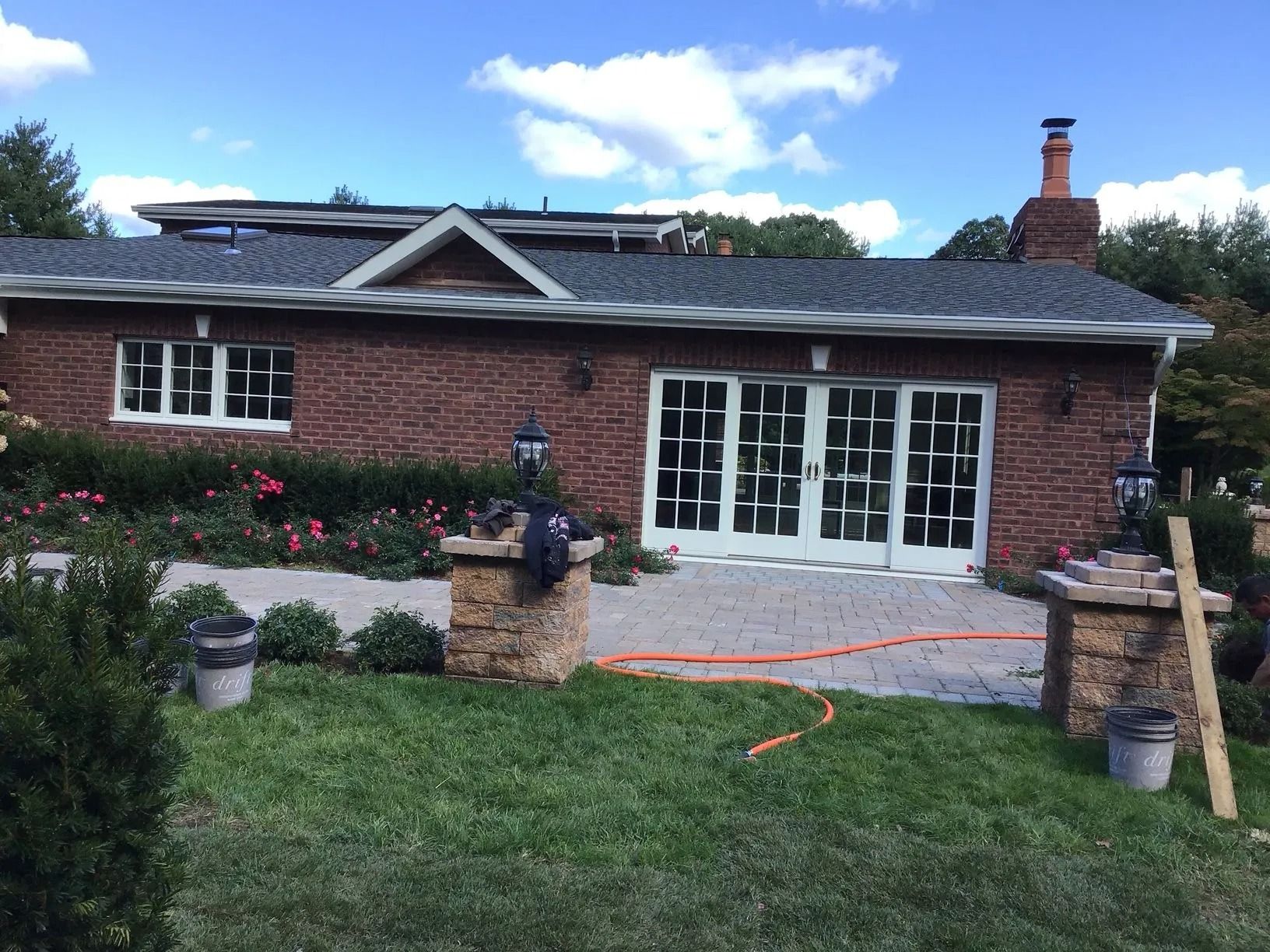 Brick house with white doors, windows, and brick pillars on a patio with a garden and blue sky.