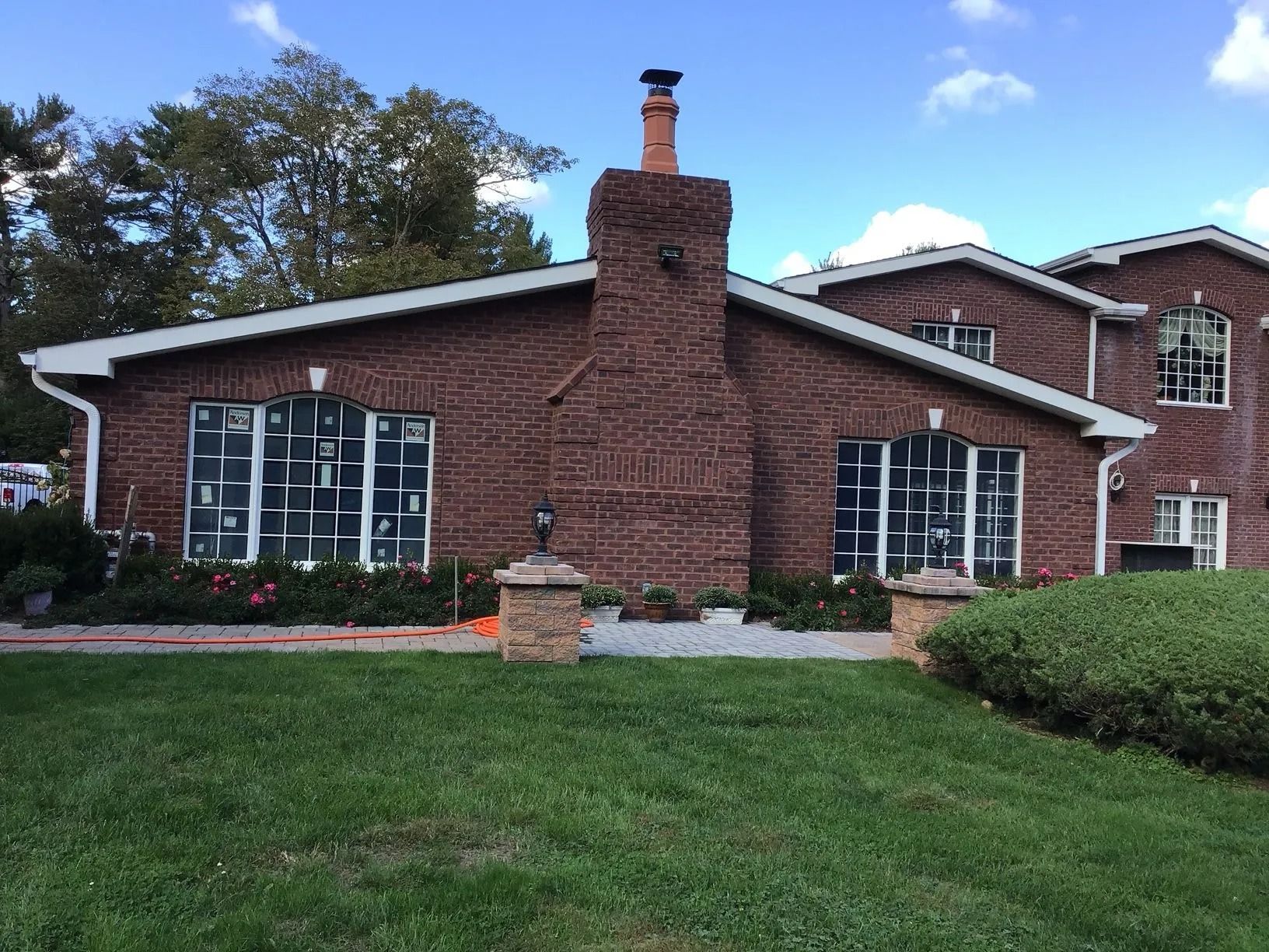 Brick building with large windows, tall chimney, and green lawn under a blue sky.