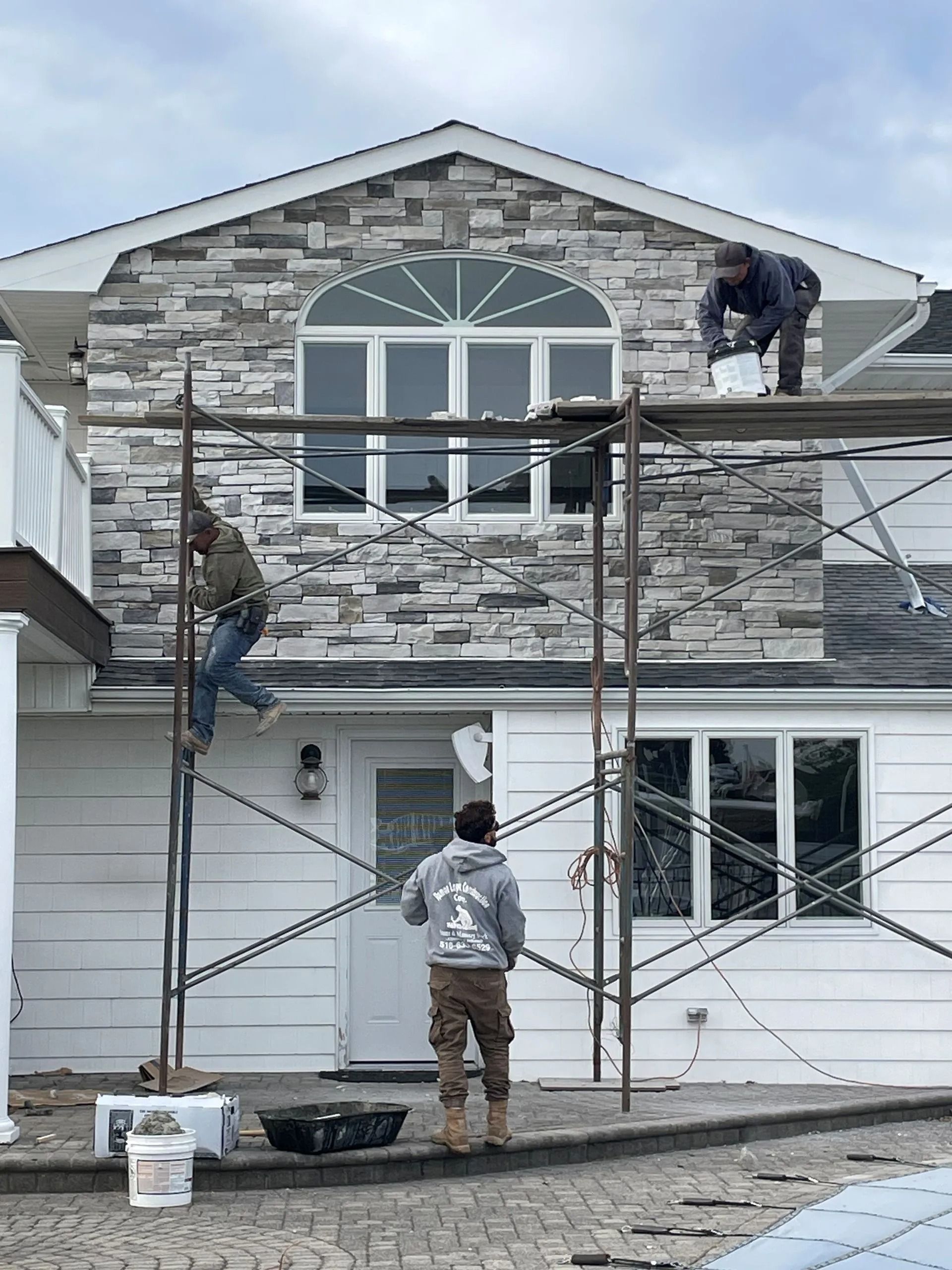 Construction workers applying stone siding to a house, using scaffolding.