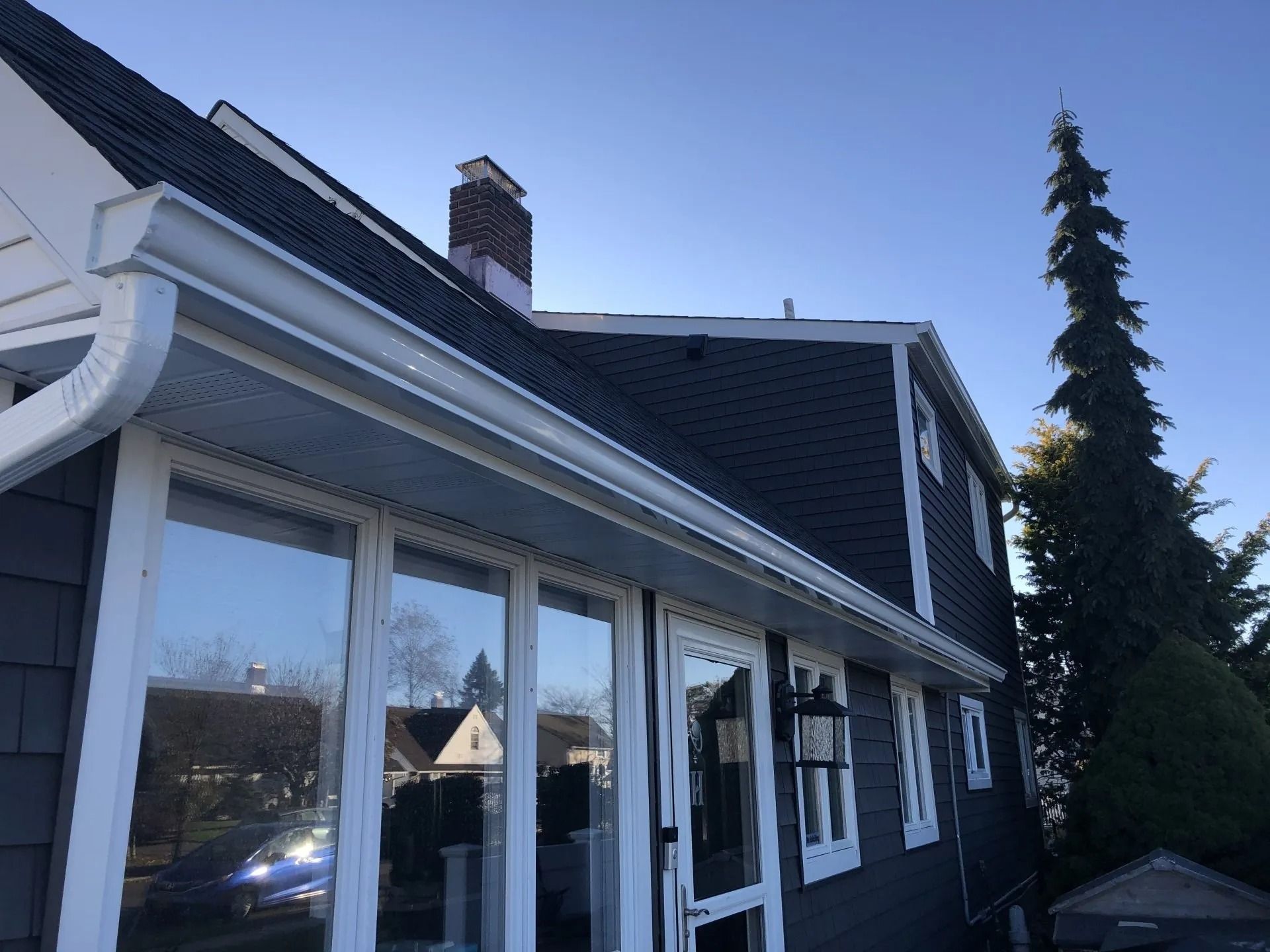 House exterior with white trim, dark roof, gutters. Windows reflect the sky.