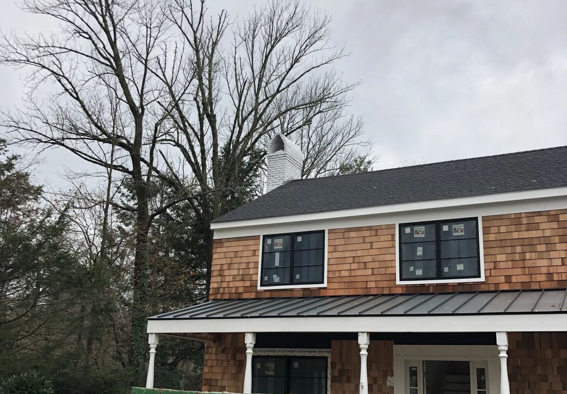 Two-story house with cedar shake siding and dark roof, windows, and trim; cloudy sky.