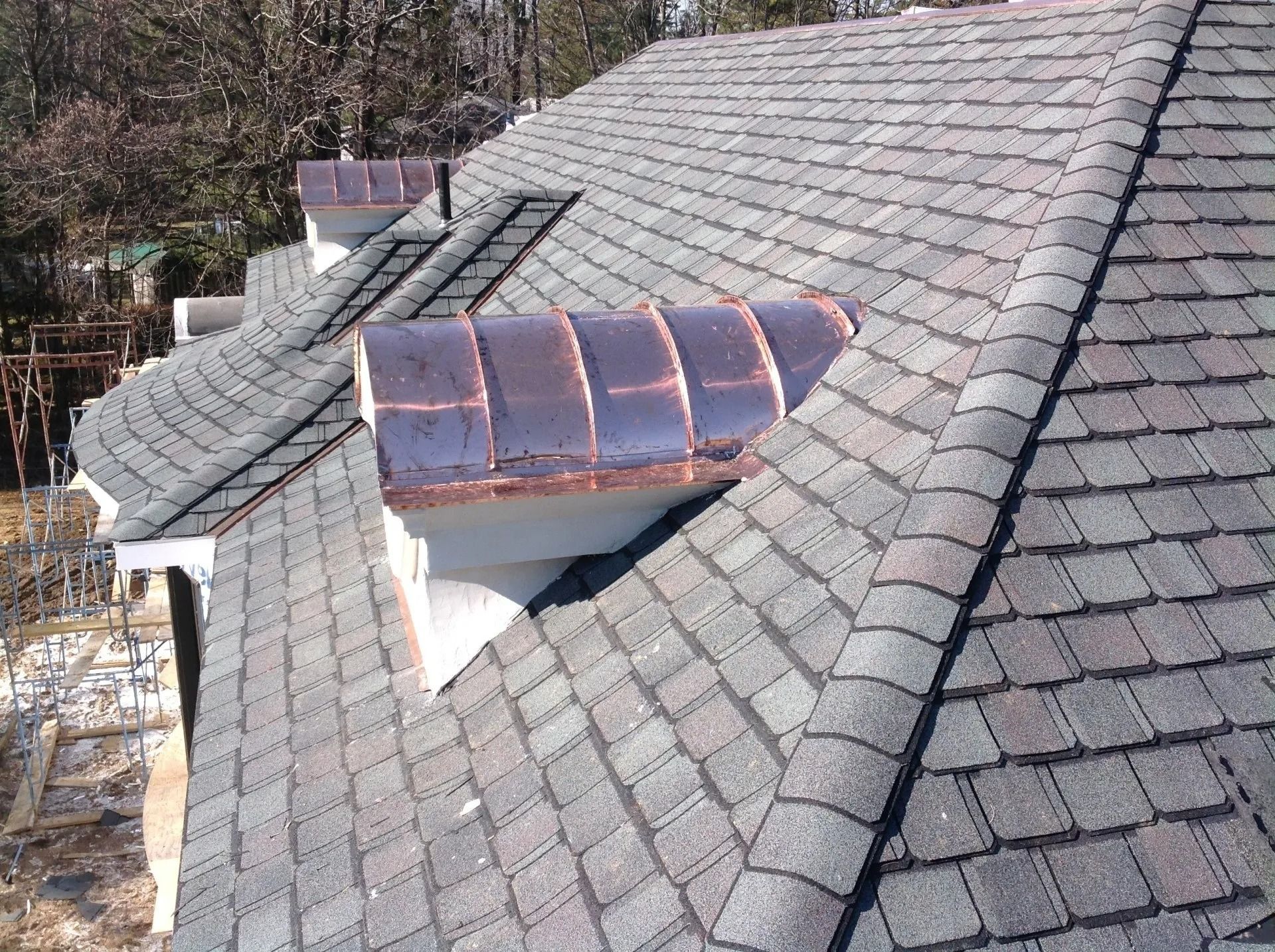 Close-up of a house roof with three copper-topped dormers. Asphalt shingles are gray.
