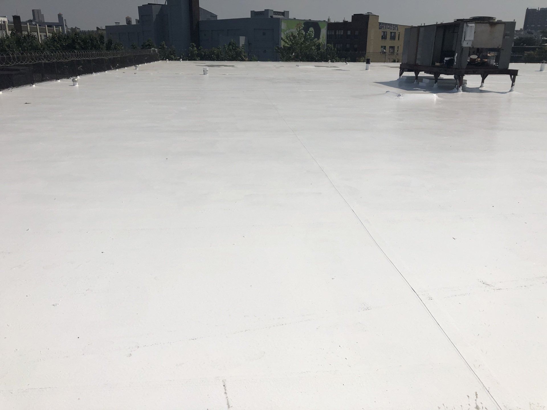 White reflective flat roof with equipment and buildings in the background.
