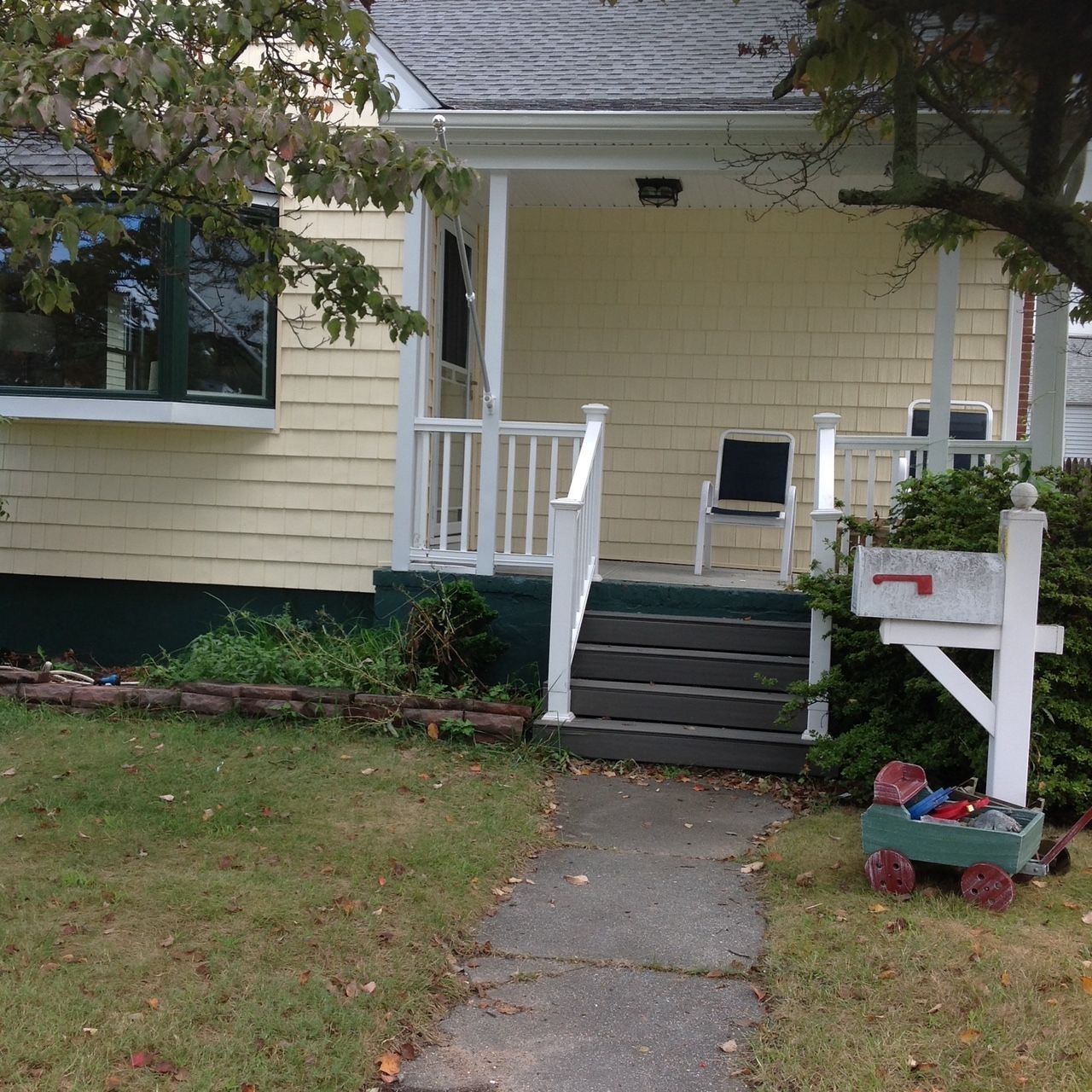 Yellow house with white porch, mailbox, and a small wagon.