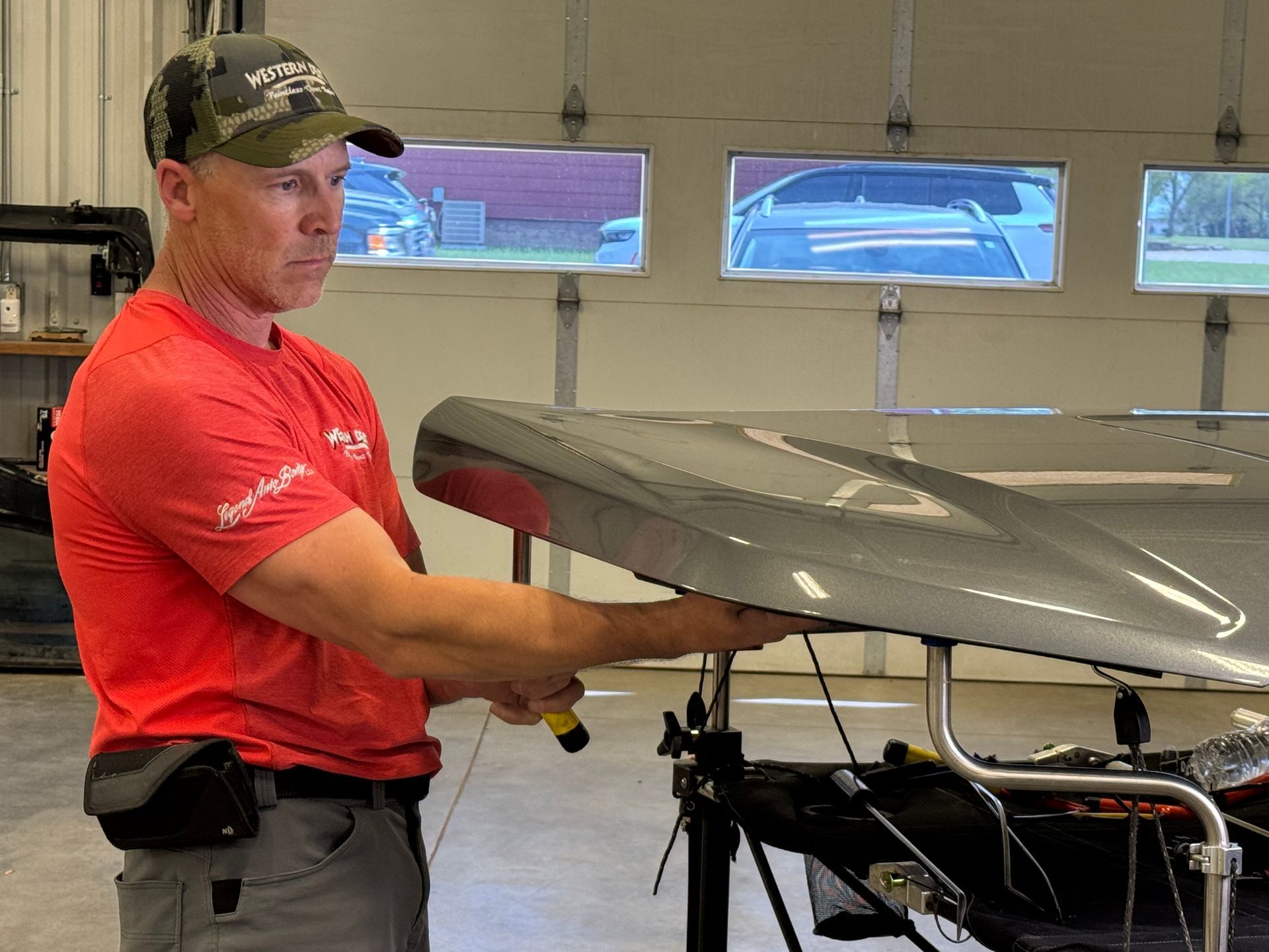 Mechanic in red shirt adjusting a car hood in a garage.